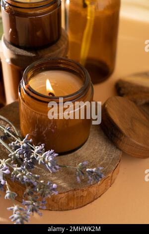 Candele di soia in un vaso di vetro. Aromaterapia. Candela e lavanda  brucianti. Coperchio in legno per vasetti. Sfondo beige. Comfort e relax.  Fatto a mano. Decorazioni per la casa Foto stock 