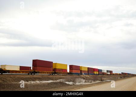 Carrozze rosse, arancioni e gialle su un letto piano lungo un binario ferroviario Foto Stock