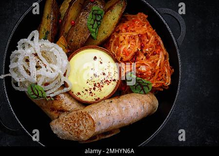 Salsicce fritte con patate al forno, cavolo in umido, in padella, su cemento grigio Foto Stock