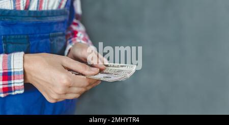 la donna conta banconote da un pacchetto di denaro con una denominazione di 50 dollari su sfondo grigio e blu. la lavoratrice della donna sta tenendo le fatture del dollaro nella sua h Foto Stock