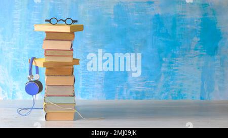 concetto di audiolibro con grande pila di occhiali da libro e cuffie vintage, sfondo di vernice blu Foto Stock