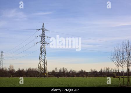 Campo coltivato con piloni elettrici e cavi di testa in una giornata nuvolosa nella campagna italiana Foto Stock