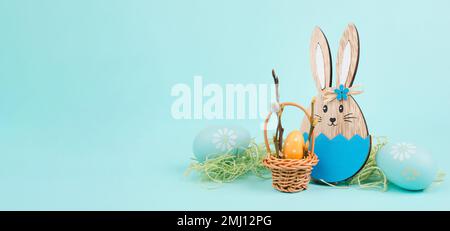 Coniglietto di Pasqua o coniglio seduto accanto a un cesto di vimini pieno di uova colorate, vacanze primaverili Foto Stock