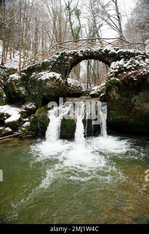 Cascata Scheissendempel, fiume Nero Ernz con ponte in pietra coperto di neve, percorso Mullerthal a Waldbillig, Lussemburgo in inverno Foto Stock