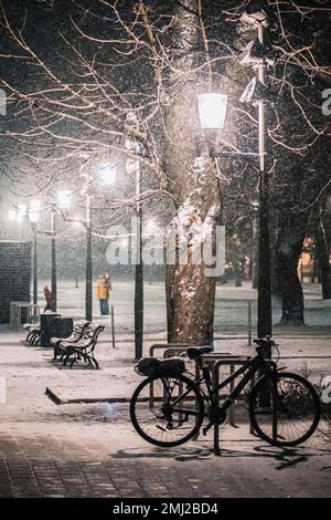 Bella scena invernale in un parco della città vecchia di Vilnius con persone che camminano nella tempesta, alberi, lampioni di strada, panchine e una bicicletta coperta dalla neve Foto Stock