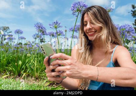 ritratto di giovane donna latina di etnia colombiana, capelli lunghi, abiti blu, sorridente, divertito seduto nel parco a riposo con il telefono, con volata Foto Stock