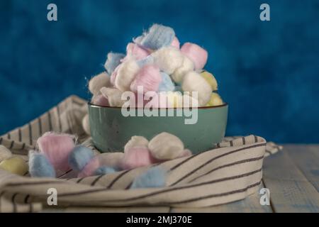 Palline di cotone colorate in vari contenitori su sfondo blu Foto Stock