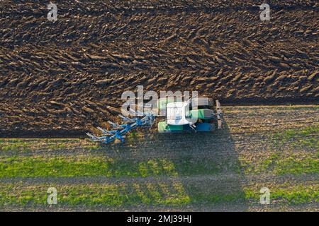 Trattore con aratro, macchina aratrice agricola che lavora su un campo in primavera Foto Stock