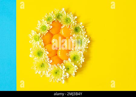 Tuorli crudi freschi disposti a forma di uovo decorato con fiori su sfondo giallo. Concetto di Pasqua insolito. Cibo contenente proteine. Foto Stock