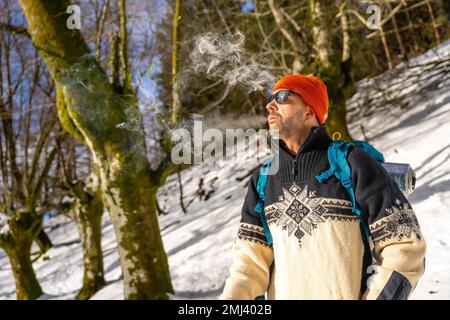 Un uomo che fuma una sigaretta su una collina innevata in inverno, godendosi il fumo freddo Foto Stock