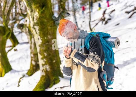 Un uomo che fuma accendendo una sigaretta con un accendisigari su una montagna innevata in inverno Foto Stock