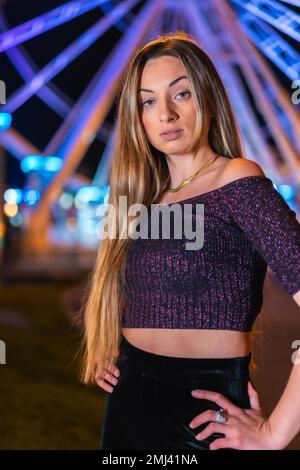 Natale in città di notte, decorazione in inverno. Ragazza bionda sorridente su una ruota panoramica illuminata Foto Stock