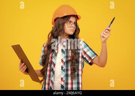 Bambino pittore adolescente in casco con clipboard. Bambino in elmetto. Ingegnere di capretto sul luogo di costruzione. Ristrutturazione e riparazione. Pensare intelligente pensivo Foto Stock