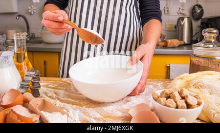 Confetter donna in un grembiule culinario a strisce mescolando gli ingredienti con un cucchiaio mentre si cucinano i biscotti di pan di zenzero di Natale, primo piano Foto Stock