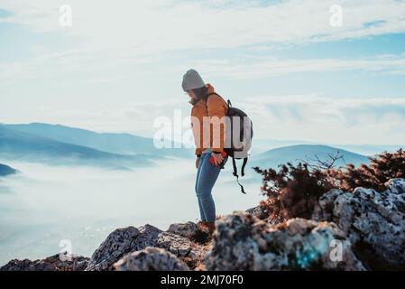 una ragazza escursionistica con uno zaino sulla schiena guarda la mattina dalla cima della montagna Foto Stock