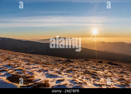 Paesaggio sulla faccia sud della Sierra Nevada all'alba, collina con piante e neve e il sole che sorge sullo sfondo delle montagne.Granada Foto Stock