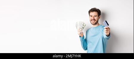 Sorridente uomo caucasico tenendo i soldi e dandogli carta di credito plastica, in piedi su sfondo bianco Foto Stock