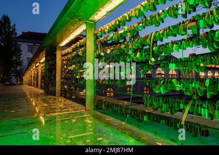 Primo piano delle chiuse d'amore sul ponte dei macellai al crepuscolo con le luci del ponte sul canale del fiume Lubiana in Slovenia Foto Stock