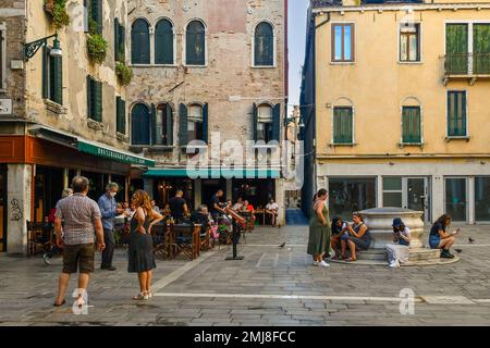 Turisti in campo Sant'Aponal (Piazza San Apollinaris) con ristoranti all'aperto e un tipico pozzo veneziano, Venezia, Veneto, Italia Foto Stock