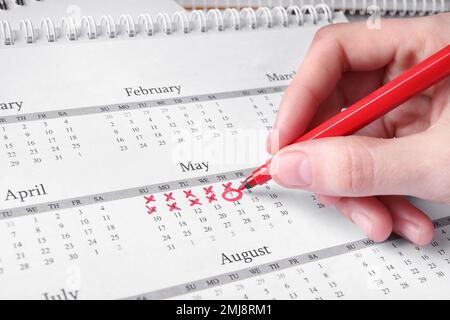 Donna che segna la data in calendario con pennarello rosso, primo piano Foto Stock