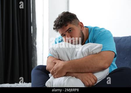 Un uomo in sovrappeso depresso che abbraccia il cuscino sul letto Foto Stock