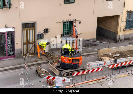 Lavori di manutenzione idraulica in una strada, centro di Firenze. Scavare il terreno con il caricatore retroescavatore. Lavoratore con pala. Società di acqua Publiacqua. Foto Stock