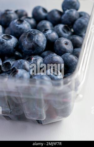 primo piano di mirtilli freschi in una scatola di plastica, tavolo bianco Foto Stock