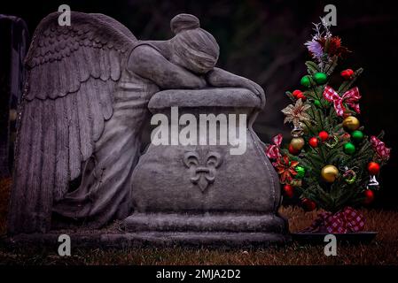 Un albero di Natale si trova accanto ad un angelo piangente in San Rose of Lima Cemetery, 1 gennaio 2023, a Coden, Alabama. Foto Stock