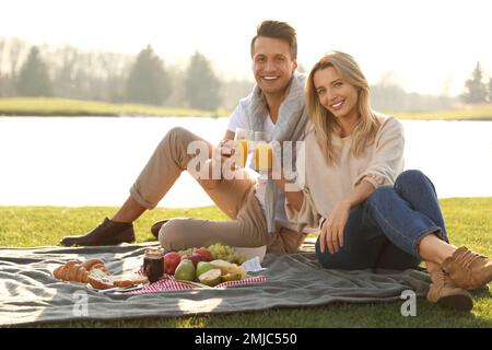 Felice giovane coppia che ha pic-nic vicino al lago nella giornata di sole Foto Stock