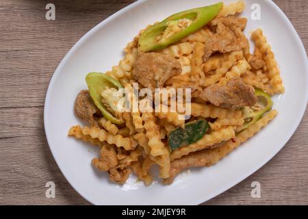 In un piatto bianco, mescolare il maiale fritto con la pasta di curry rosso e i giovani germogli di cocco Foto Stock