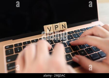 Mani utente che digita sulla tastiera del computer portatile con parola VPN su cubi di legno primo piano. Foto Stock