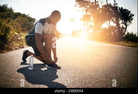 Mostra, allacciati e mettiti in moto. un giovane uomo in forma che legava le scarpe prima di una corsa all'aperto. Foto Stock