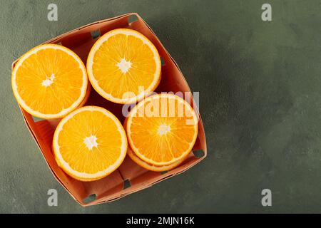 Metà arance in un cesto di legno. Frutta d'arancia tagliata su fondo verde. Spazio di copia. Vista dall'alto Foto Stock