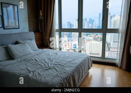 un letto rifatto vicino ad una grande finestra che si affaccia sul centro della città. Foto Stock
