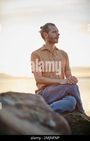 Scopri la bellezza in ogni momento. un uomo tranquillo seduto su una roccia in spiaggia. Foto Stock