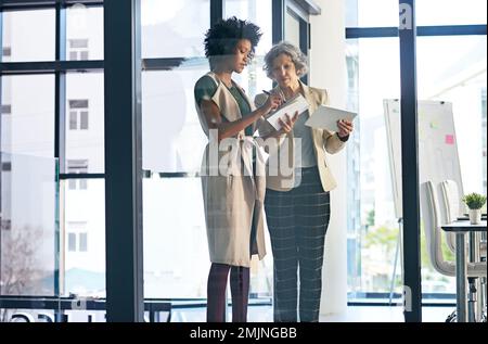 Insieme sono imbattibili. due donne d'affari che fanno appunti mentre discutono qualcosa su un tablet. Foto Stock