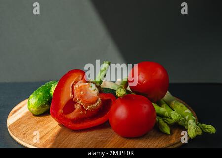 rami di asparagi verdi freschi, peperoni, pomodori e cetrioli su un asse di legno, sfondo grigio scuro, vista dall'alto. Concetto di trend di base con copia sp Foto Stock