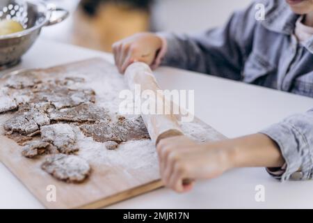 Mano della bambina che fa i biscotti tradizionali di Natale. Pasta cruda e taglierine per i biscotti da vacanza su un tavolo scuro. Preparare il gingerbrea di Natale Foto Stock