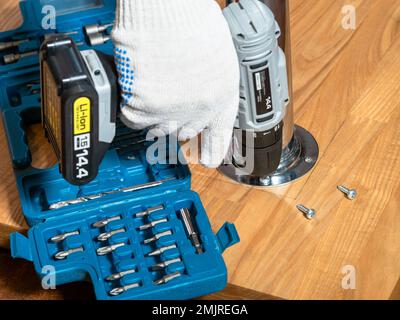 falegname avvitando la gamba metallica sul tavolo di legno utilizzando un cacciavite elettrico da vicino Foto Stock