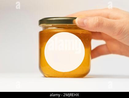 La mano di una donna mette un vasetto di miele sul tavolo con un adesivo rotondo con il taglio del plotter. con spazio per il design dell'imballaggio Foto Stock