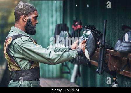 Paintball uomo, preparare maschera di sicurezza e vestiti con gli attrezzi, mimetizzazione e iniziare per il gioco di combattimento all'aperto. African guy, giochi di guerra o avventura per Foto Stock