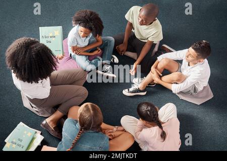 Insegnante, narrazione di storie o ragazzi in aula o in biblioteca per imparare lo sviluppo, le capacità di ascolto. Vista dall'alto, gruppo o studenti con un Foto Stock