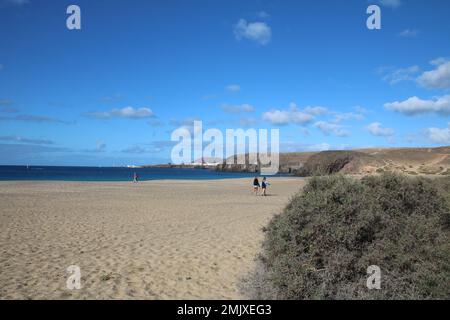 persone lontane che camminano su una spiaggia quasi deserta con cielo blu Foto Stock