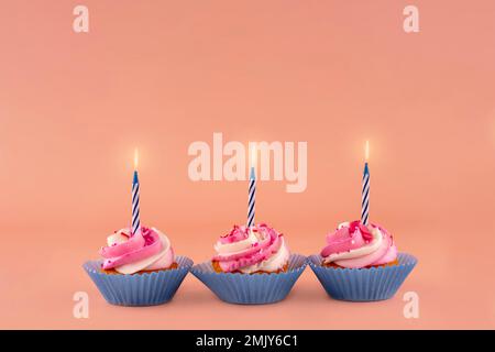 tre muffin di compleanno alle bacche in involucri blu con candele colorate su sfondo rosa foto di alta qualità per calendario e biglietti. Spazio per il testo Foto Stock