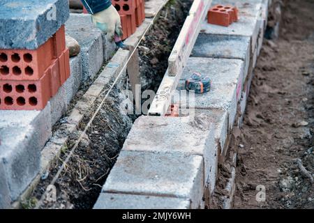 Muratore duro lavoro posa blocchi di calcestruzzo sulla parte superiore di fondazione in cemento su nuovo sito residenziale di alloggi. Combattere la crisi immobiliare costruendo più af Foto Stock