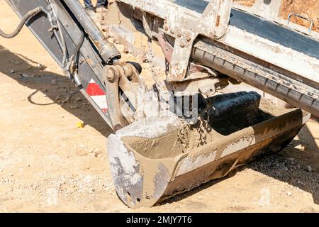 Betoniera per calcestruzzo che versa calcestruzzo fresco umido nella benna degli escavatori in un cantiere edile Foto Stock