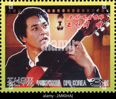 Francobollo nordcoreano del 2008 raffigurante una scena del film "Stella della Corea" con un uomo che suona la chitarra, filatelia della Corea del Nord. Foto Stock