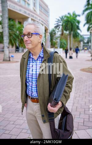 Foto di un professore universitario che cammina nel campus con persone sfocate sullo sfondo Foto Stock