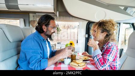 Una coppia felice che trascorre del tempo insieme divertendosi durante il pranzo all'interno di un veicolo camper in viaggio gratuito in vacanza su strada. Persone con auto da campeggio h Foto Stock