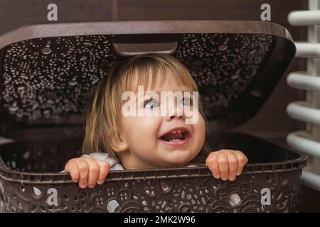 adorabile bambino che si nasconde in un cesto di bucato Foto Stock